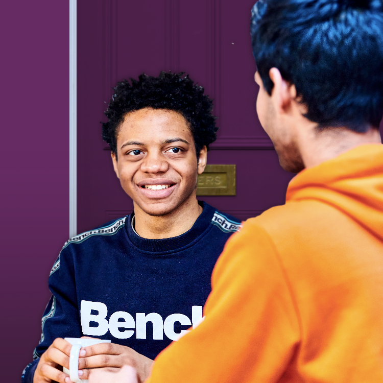 TA male student with a hot drink talking to another person facing away from the camera, in front of a purple house door