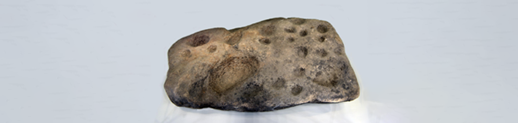 Colour photograph of a large rock covered with prehistoric ‘cup and ring’ marks.