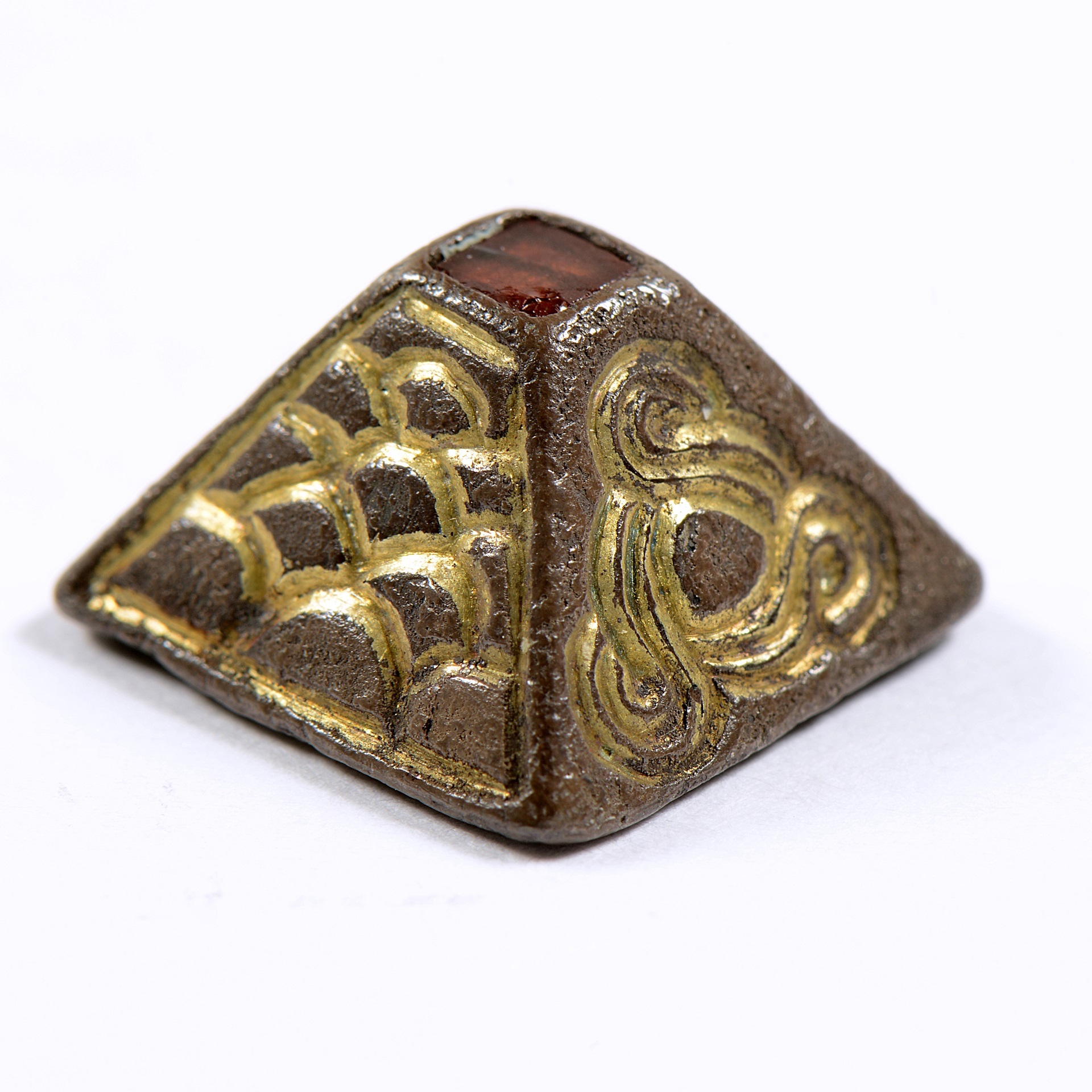 A silver Anglo-Saxon pyramid mount, inlaid with a single garnet and with gold decoration on white background.