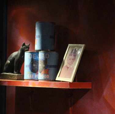Part of art installation including an ancient Egyptian cat model, modern cat food tins, a photograph and the painted words ‘dust to dust’ on the background.