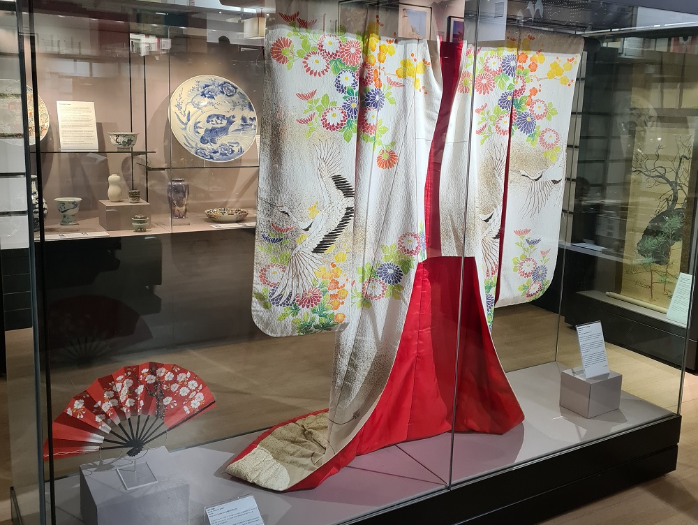 view through a museum display case with a kimono hanging in it to displays behind